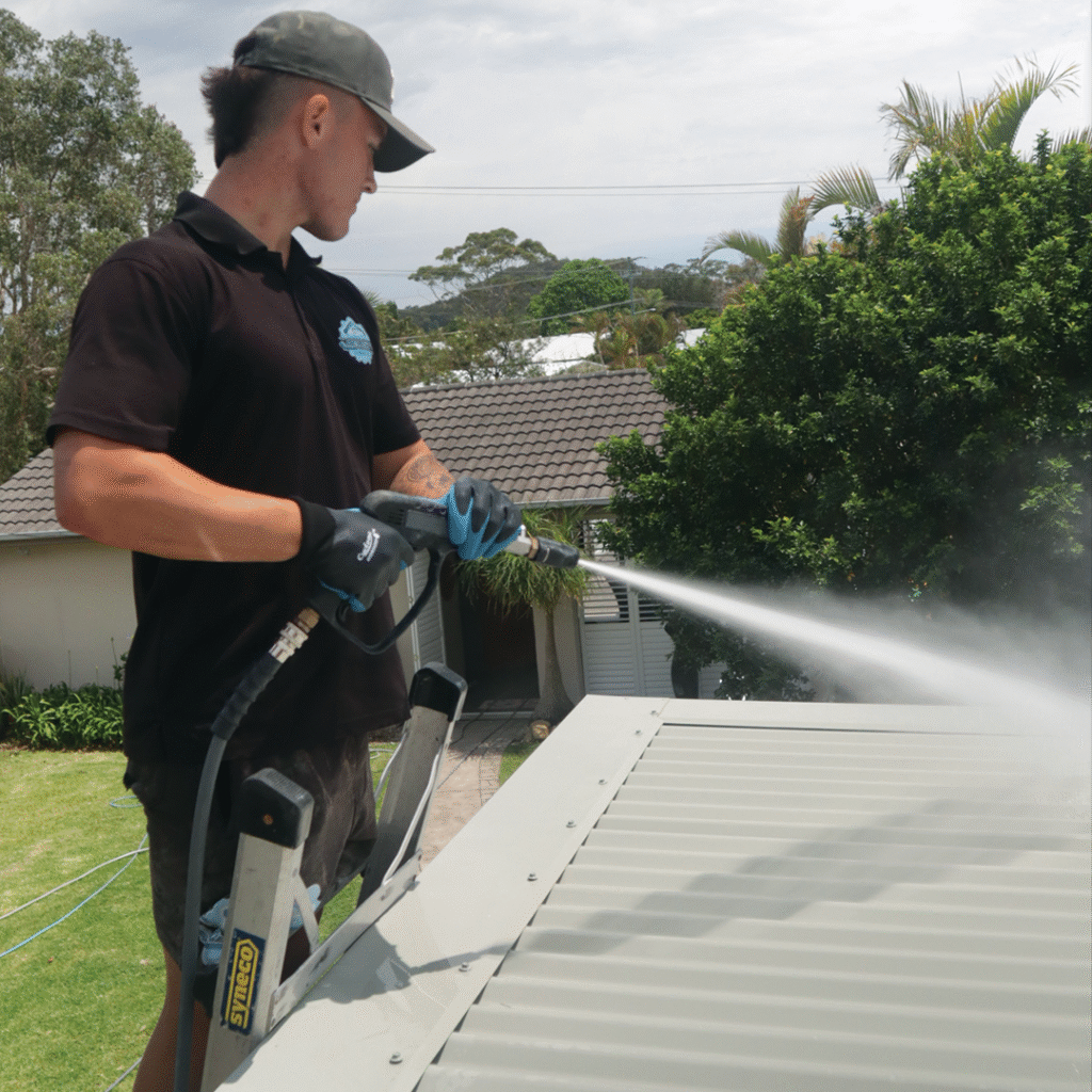 Roof cleaning in progress with a worker removing dirt and buildup from roof tiles